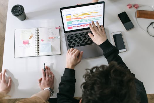 A person working on their laptop with a time blocking planner next to them